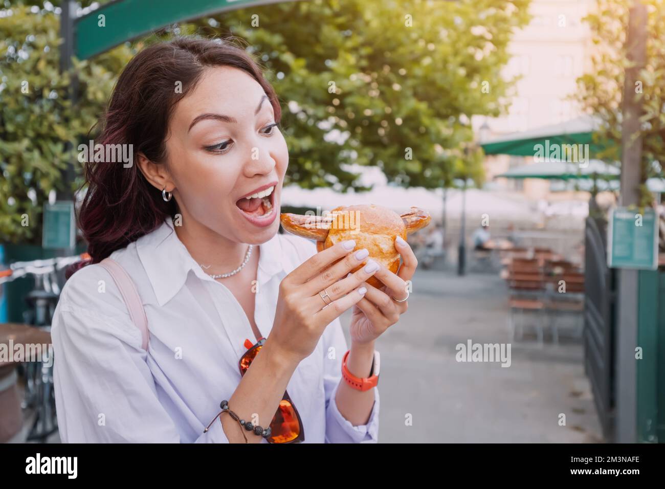 A happy girl eats an appetizing traditional German bratwurst hot dog with juicy sausage and seasonings Stock Photo