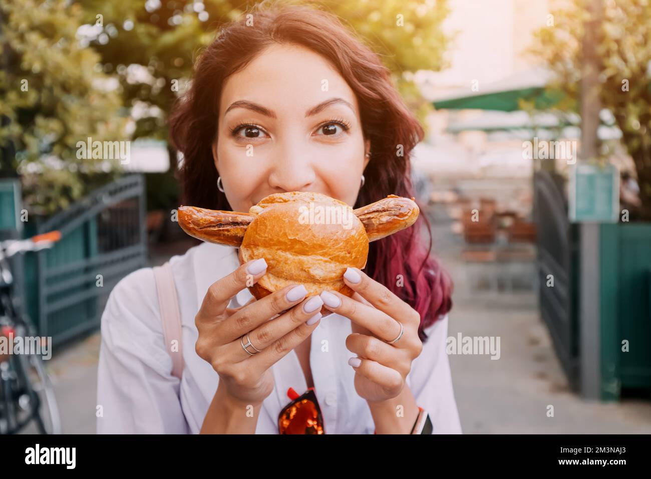 A happy girl eats an appetizing traditional German bratwurst hot dog with juicy sausage and seasonings Stock Photo