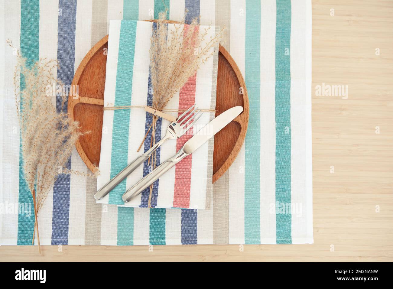 Elegant table place setting, wooden plate with decor on striped napkin and cutlery. Copy space for text Stock Photo