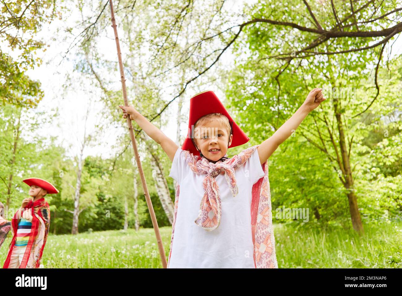 Portrait of smiling boy wearing tricorn hat with arms outstretched in green park Stock Photo