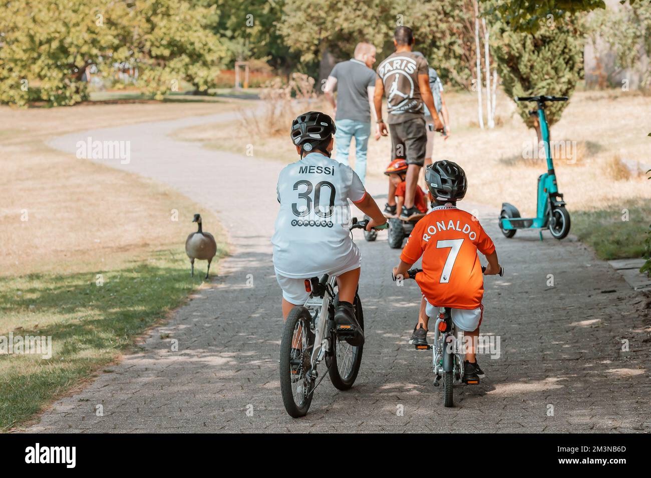 30 July 2022, Cologne, Germany: Two children friends ride bicycles in the park and compete like Messi versus Ronaldo with their numbers and names on T Stock Photo