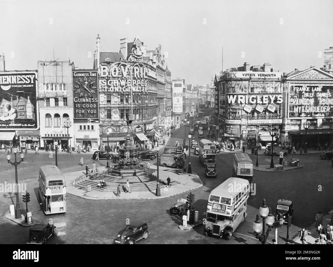 Piccadilly Circus, London, with buses and cars rounding the Statue of Eros. Rainbow Round My Shoulder starring Frankie Laine and Billy Daniels is showing at the London Pavilion. Illuminated advertisements include Bovril, Schweppes, Guinness and Wrigley's.     Date: 1952 Stock Photo