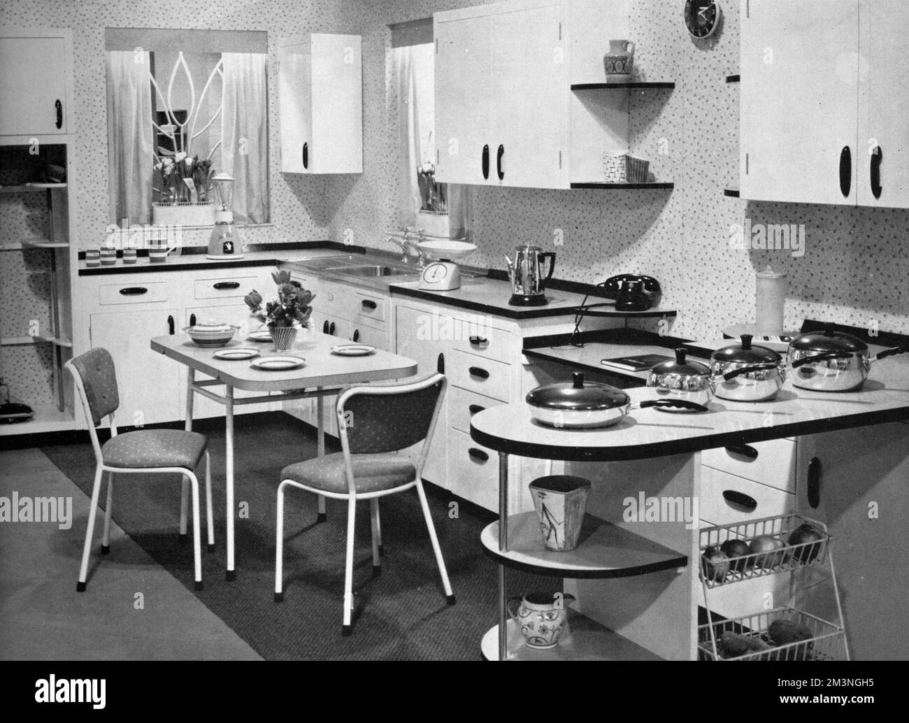 A smart Nevastane kitchen from 1957 featuring an L-shaped unit, Majestic table and chairs and various cabinets.  Also visible is a Colorama pan set, a coffee percolator, a Westclox clock, and a broom cupboard.       Date: 1957 Stock Photo