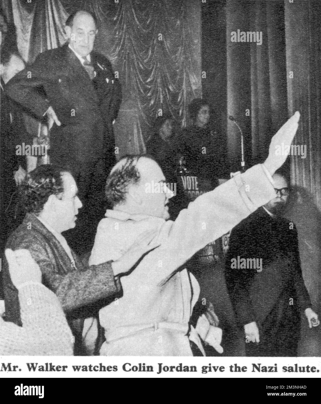 Colin Jordan, leader of the British National Socialist movement, gives the Nazi salute at a by-election meeting in Leyton, East London, watched by Labour MP Patrick Gordon Walker.     Date: 1965 Stock Photo