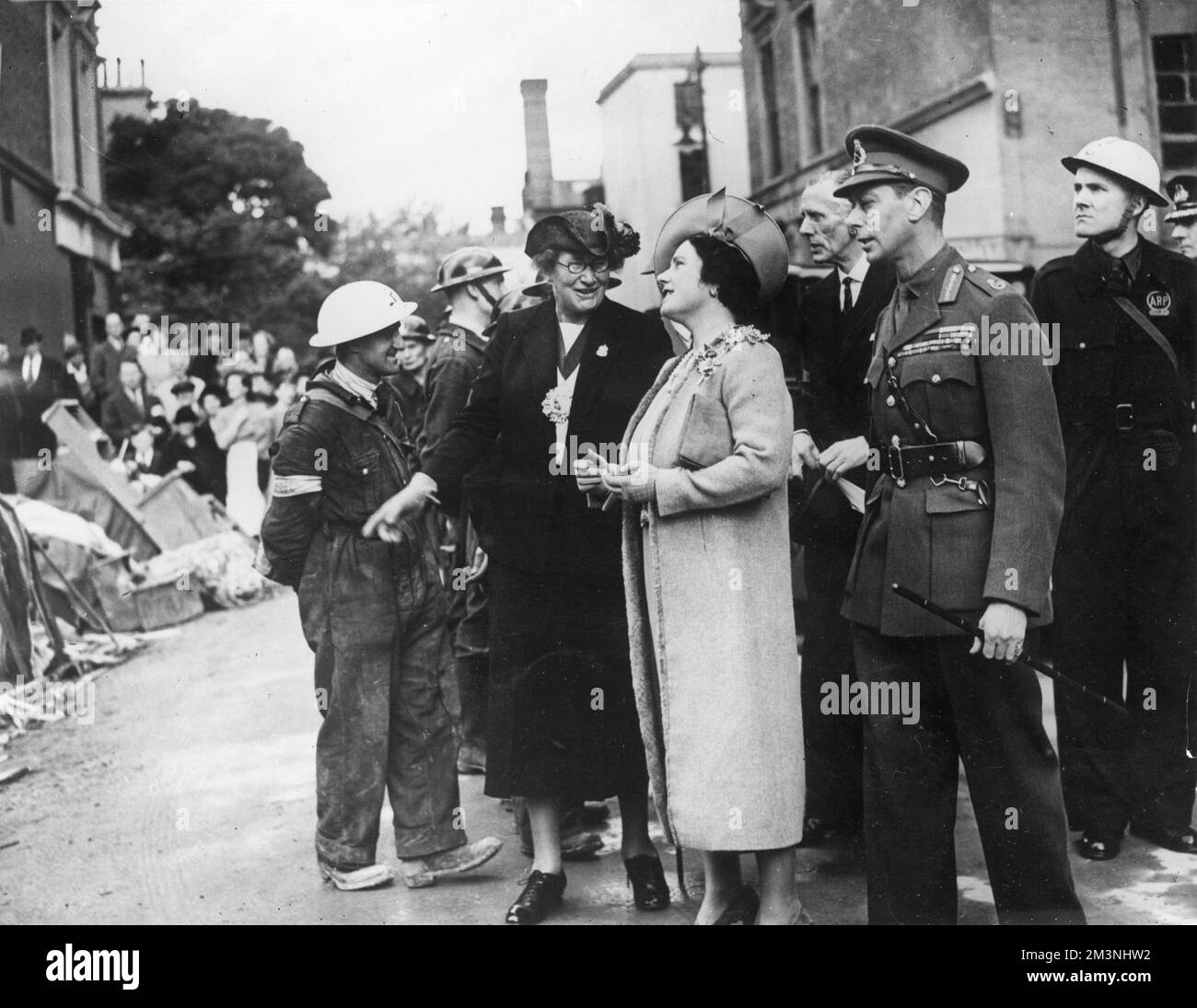 King George VI together with Queen Elizabeth chatting with Air Raid Patrol wardens and inspecting bomb damage in South West London during the Blitz, 1940.     Date: 1940 Stock Photo