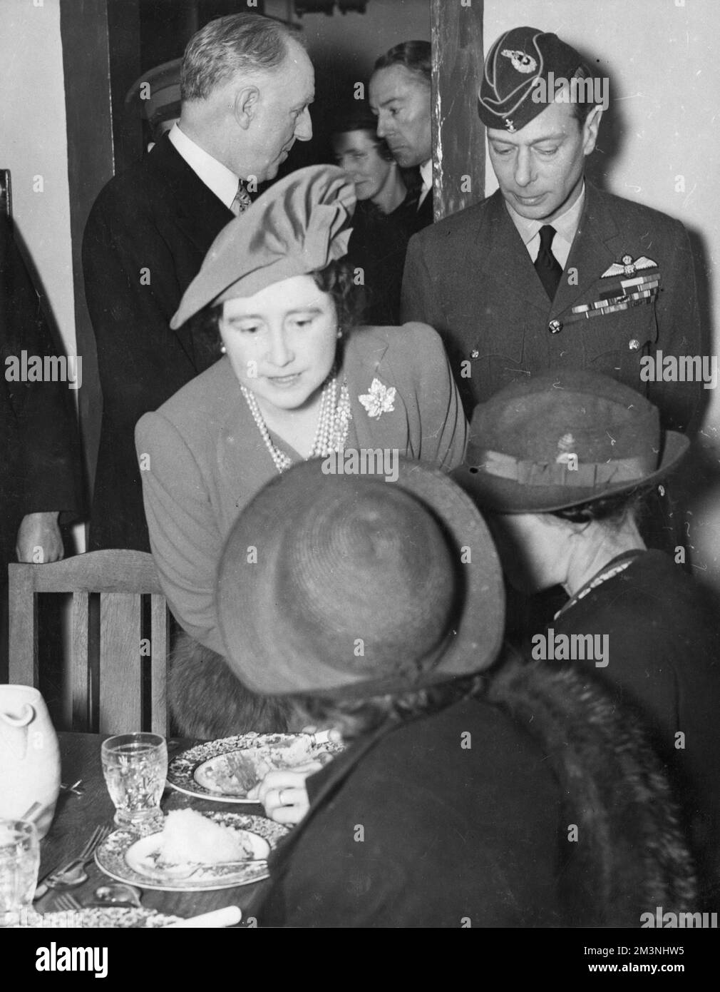 King George VI and Queen Elizabeth pictured visiting a communal centre established in South London during the Blitz to provide meals for people who had been bombed out of their homes by German air raids.  The King is in  RAF uniform.     Date: 1940 Stock Photo