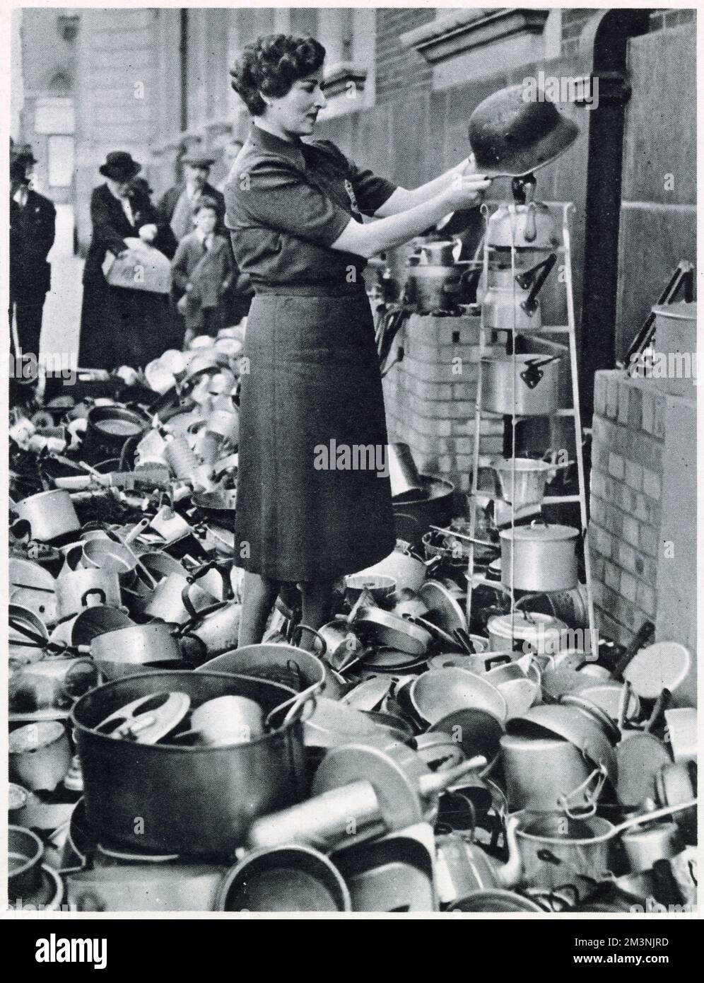 Lord Beaverbrook the Minister for Aircraft Production appealed for objects wholly or partly made of aluminium for the manufacture of aeroplanes. Photograph of a woman from the from the Women's Voluntary Service outside their town hall, surrounded by kitchen utensils including a German steel helmet from World War One. Stock Photo