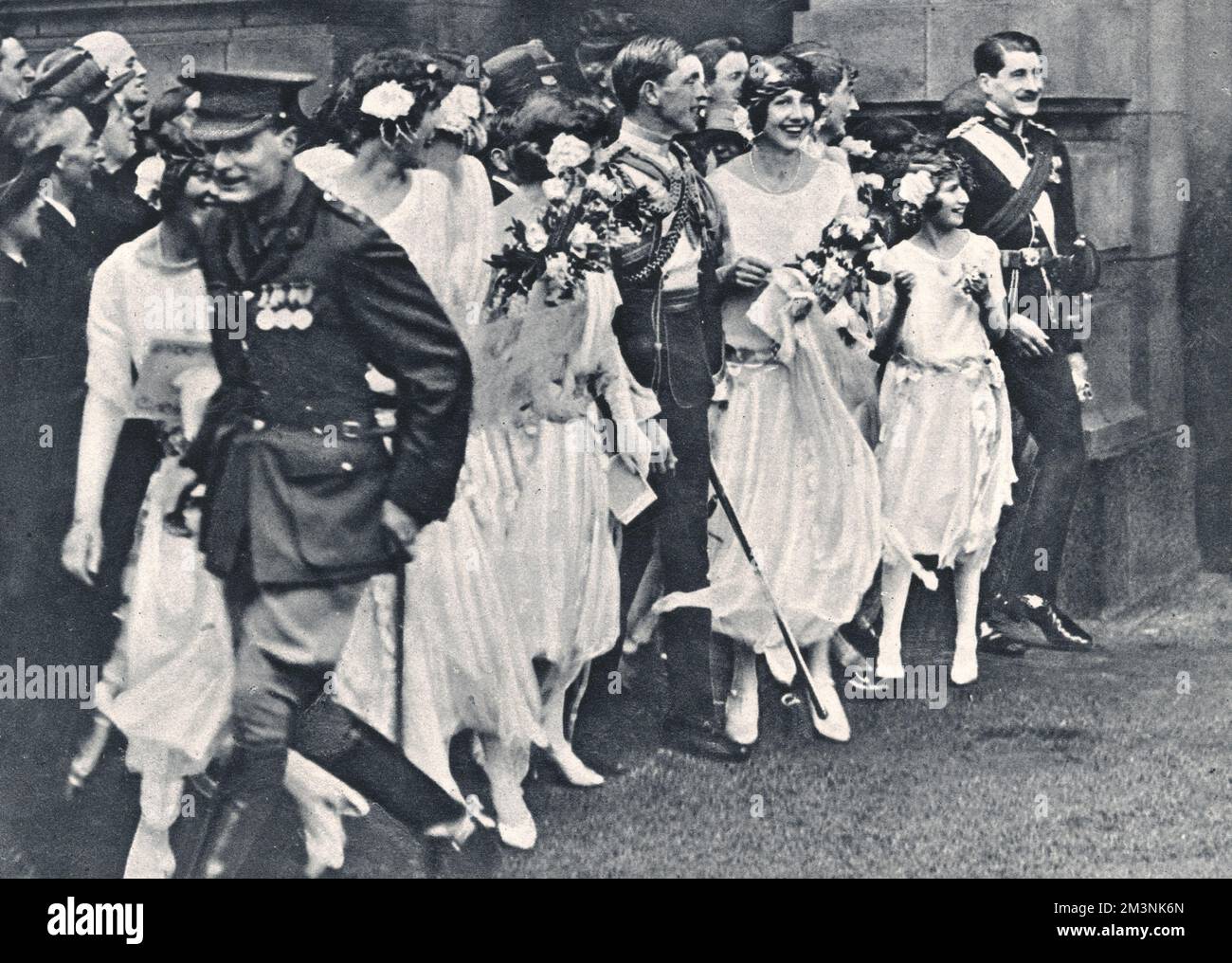 A group of wedding guests line up to bombard the newlywed Duke and Duchess of York with rose leaves as they depart for their honeymoon from Buckingham Palace courtyard for their honeymoon.  The group includes bridesmaids, Lady Katherine Hamilton, The Hon. Cecilia Bowes-Lyon and the Hon. Diamond Hardinge.     Date: 1923 Stock Photo