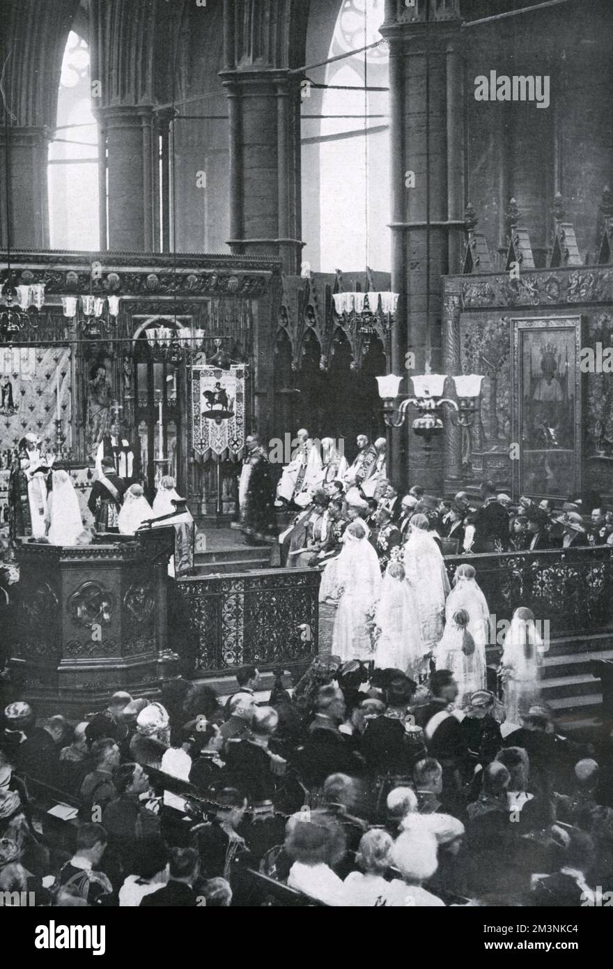 Inside Westminster Abbey during the marriage service of Princess Mary, only daughter of King George V and Queen Mary, later Princess Royal and Countess of Harewood, to Viscount Lascelles, later 6th Earl of Harewood. The couple are kneeling and being addressed by the Archbishop of Canterbury, Randall Davidson. On the first row of chairs are seated King George V, Queen Mary, the Duke of York (later George VI), and the Duchess of Fife, at this point holding the title Princess Royal.     Date: 28th February 1922 Stock Photo