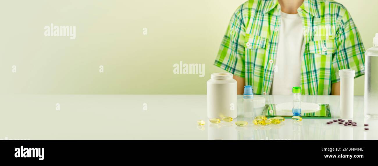Oftalmology banner with boy siting at the table with containers with contact lenses, eye drops, clean solutions and vitamins for good vision. Night co Stock Photo