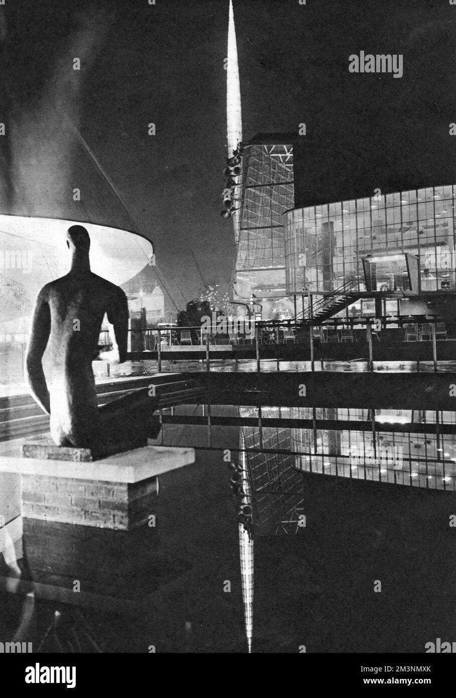 View by night of part of the Festival of Britain site on the South Bank, London.  On the left is a modern sculpture, with the Skylon rising in the centre and the Transport Pavilion on the right, both reflected in water.       Date: early 1951 Stock Photo