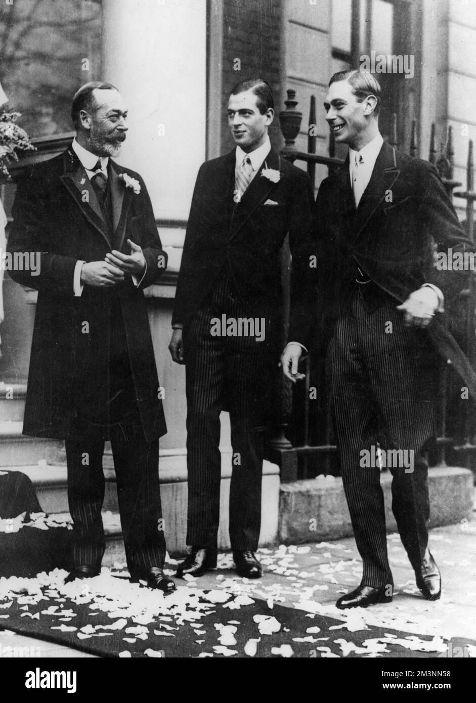 Informal photograph of King George V pictured with two of his sons, Prince George (centre), later Duke of Kent and Prince Albert, later King George VI, all at the wedding of Princess Maud of Fife, the King's niece.  The royal party had just seen the newlyweds (she married Charles Carnegie, Earl of Southesk on November 12th 1923 at the Guards Chapel) hence the confetti of petals lying on the ground.       Date: 1923 Stock Photo