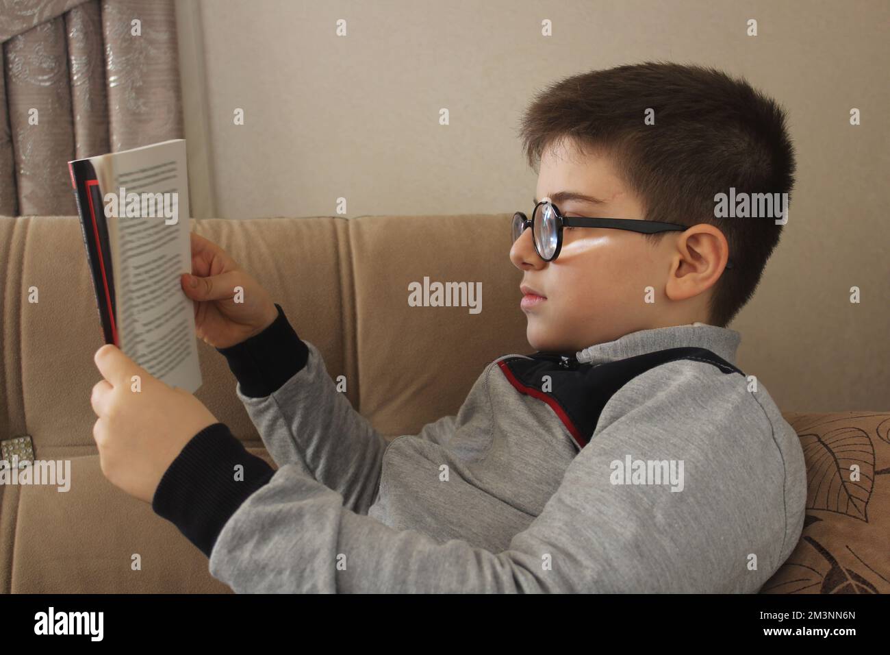 Reading book, little child in eyeglasses reading book at home in his room. Stock Photo