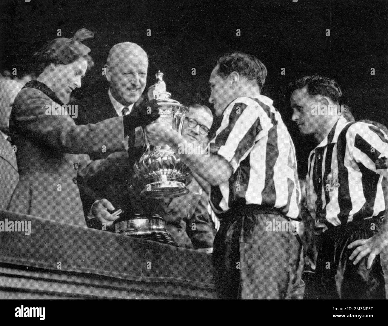 The Queen hands the F.A. Cup to the Newcastle captain, Jimmy Scoular, watched by the Secretary of the Football Association, Sir Stanley Rous. B. Cowell, the Newcastle right back, is standing on the right. Newcastle beat Manchester City 3-1 in the final.      Date: 1955 Stock Photo