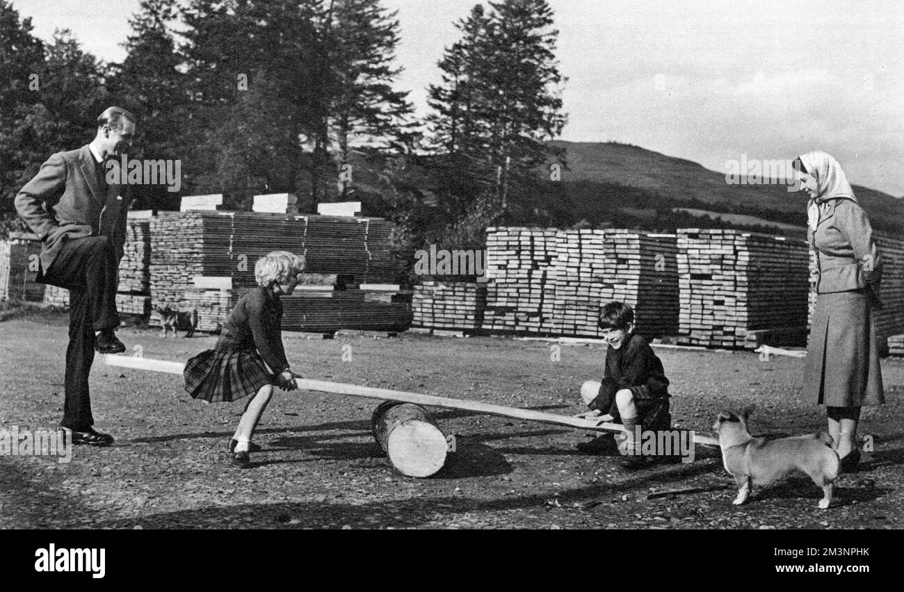 While the Queen looks on, Prince Philip, Duke of Edinburgh, rocks a see-saw for Prince Charles and Princess Anne during their visit to the farm and saw mill on the Balmoral Castle Estate in Scotland.     Date: 1957 Stock Photo