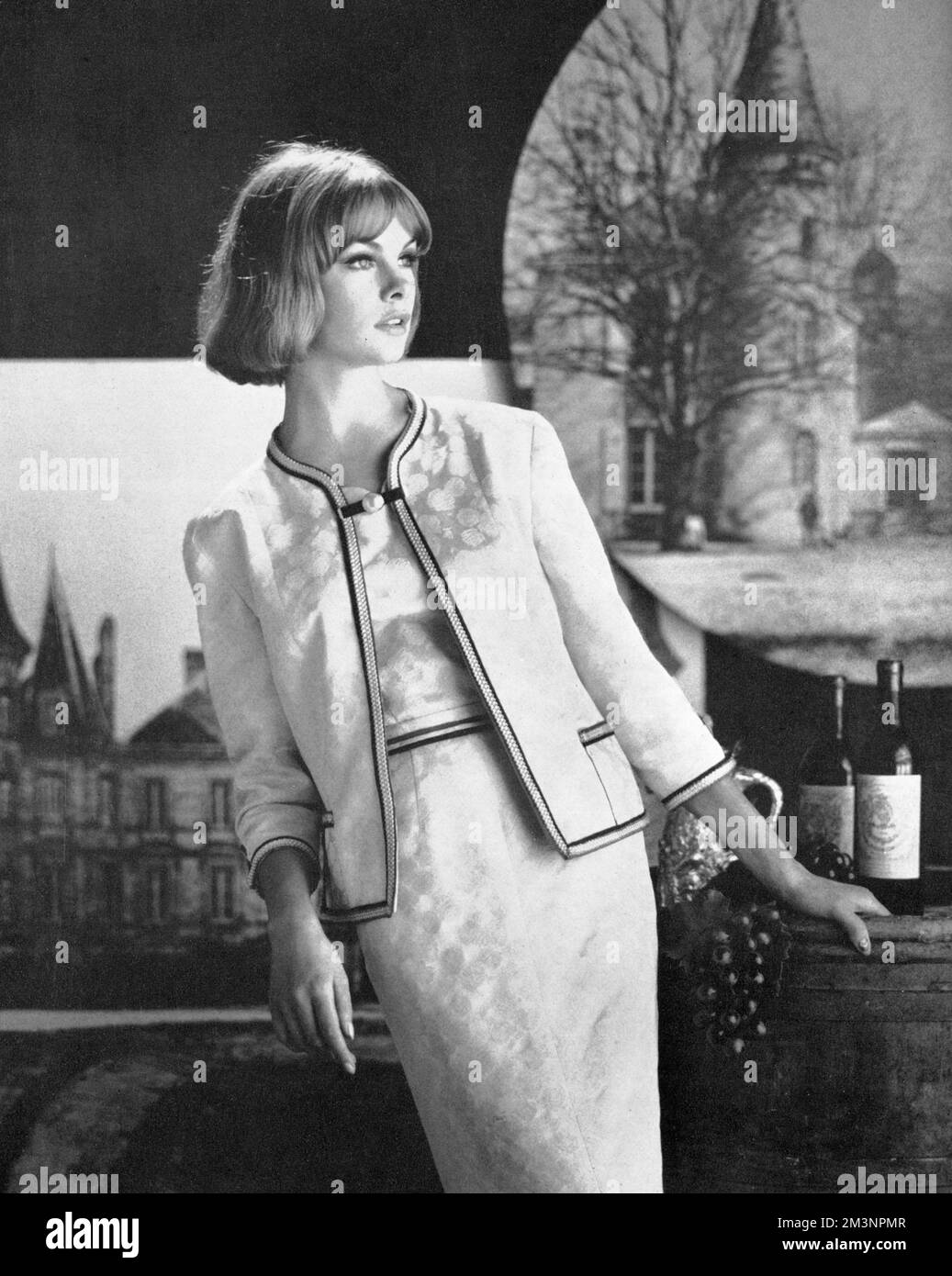 Archetypal 1960s model Jean Shrimpton, wearing an oyster white brocade dress and jacket trimmed with navy, red and gold ribbon and fastened with a gilt and pearl pin, designed by Susan Small.       Date: 1961 Stock Photo