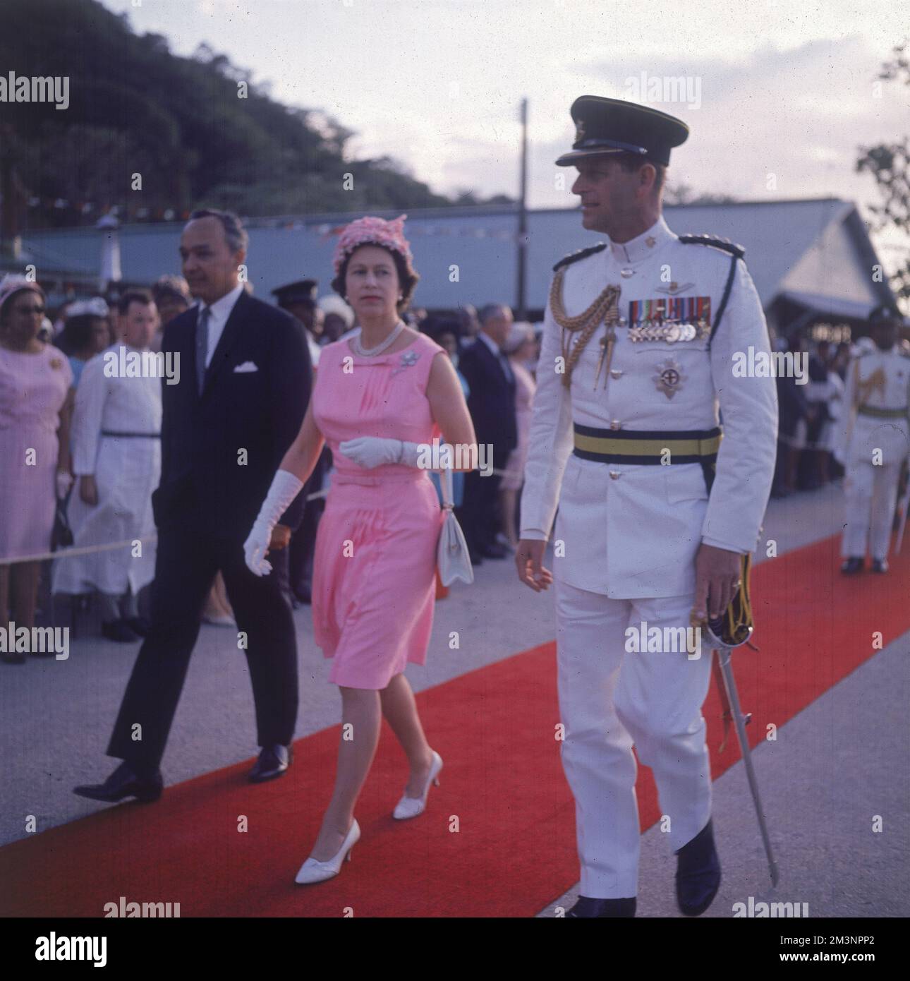 Queen Elizabeth II, wearing a striking pink outfit, pictured on her West Indies tour of 1966 accompanied by Prince Philip in a dashing white dress uniform on the red carpet.     Date: 1966 Stock Photo