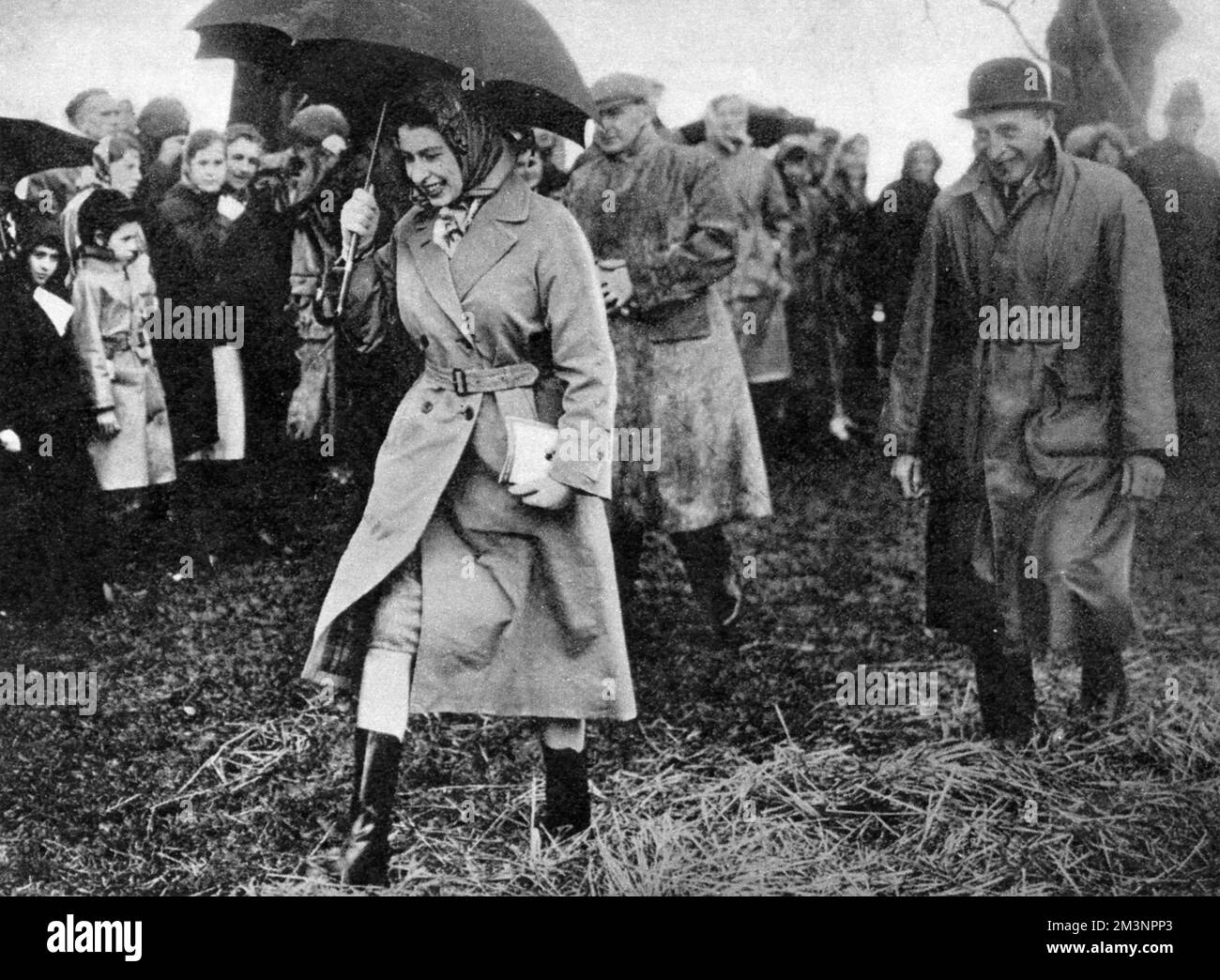 The Queen, well protected from the rain, walks across a muddy field to watch the dressage at the Badminton horse trials, 1959.     Date: 1959 Stock Photo