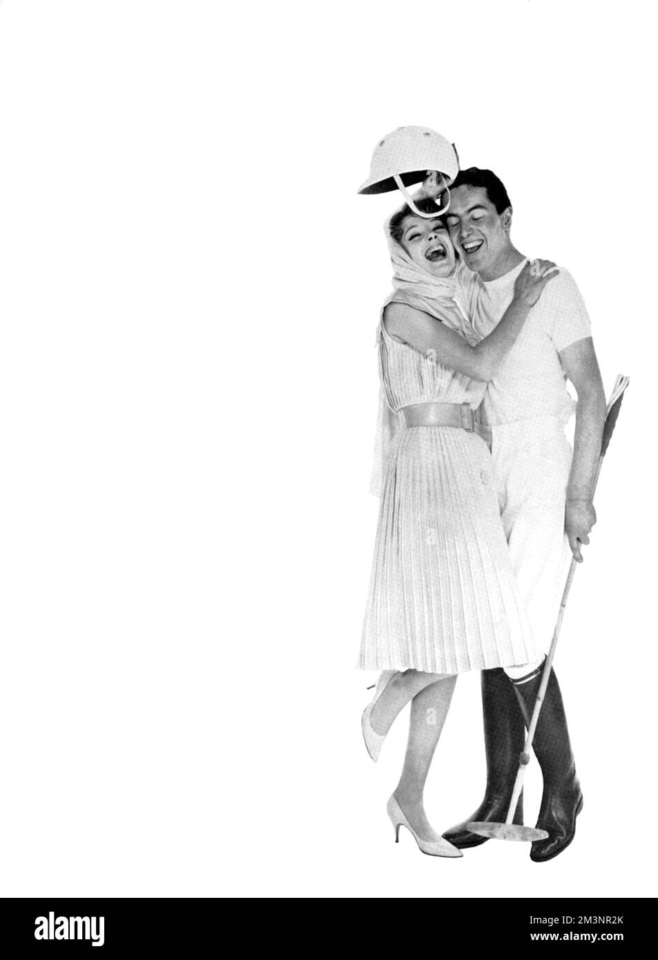 A girl hugs her polo player boyfriend wearing a casual dress by Ronald Paterson in brilliant turquoise shantung.  The dress is sleeveless, pleated throughout and cinched at the waist by a wide leather belt.  Her beau wears a polo kit from Moss Bros.     Date: 1960 Stock Photo