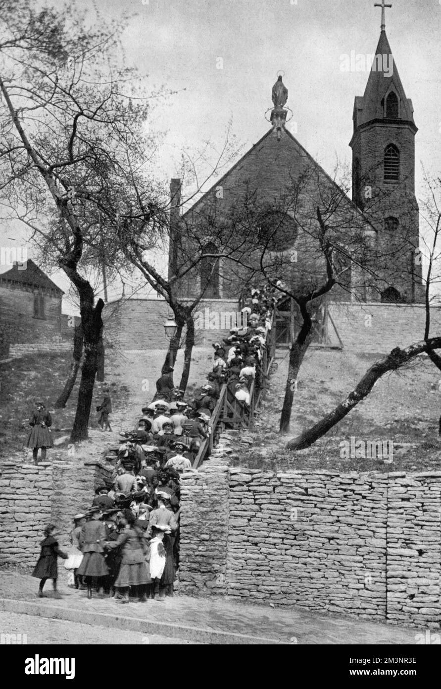 The annual pilgrimage to the Church of the Immaculate Conception, Cincinnati showing pilgims ascending the many steps up to the church.  he Immaculata Church has served since 1860 as a pilgrimage church, where on Good Friday the faithful ascend 85 steps to the church's front door from the neighborhood below while praying the Rosary. An additional 65 steps start at the base of Mt. Adams, with a pedestrian bridge over Columbia Parkway connecting the two paths. The steps were originally made of wood, but in 1911, the City of Cincinnati helped the church build concrete steps.     Date: 1909 Stock Photo