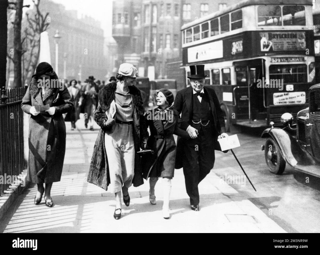 Clementine Churchill and her husband Winston walk hand in hand down a London street with their youngest daughter Mary (later Baroness Soames). They are on their way to Westminster Hall for a ceremony in which their Majesties King George V and Queen Mary will receive an address of congratulation from each house of Parliament, 9th May 1935     Date: 9th May 1935 Stock Photo