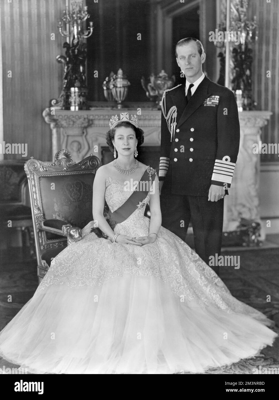 Queen Elizabeth II and Prince Philip, Duke of Edinburgh pictured together in the Grand Entrance in Buckingham Palace in 1954.  The Queen is wearing a yellow tulle evening gown decorated with sprays of mimosa and gold pailette embroidery and is wearing the blue Ribbon and Star of the Garter.  Her necklace was a wedding present from the Nizam of Hyderabad; the tiara also a wedding present from Queen Mary.  The bow brooch and drop earrings are set with diamonds.  The Duke is wearing the uniform of the Admiral of the Fleet.     Date: 1954 Stock Photo