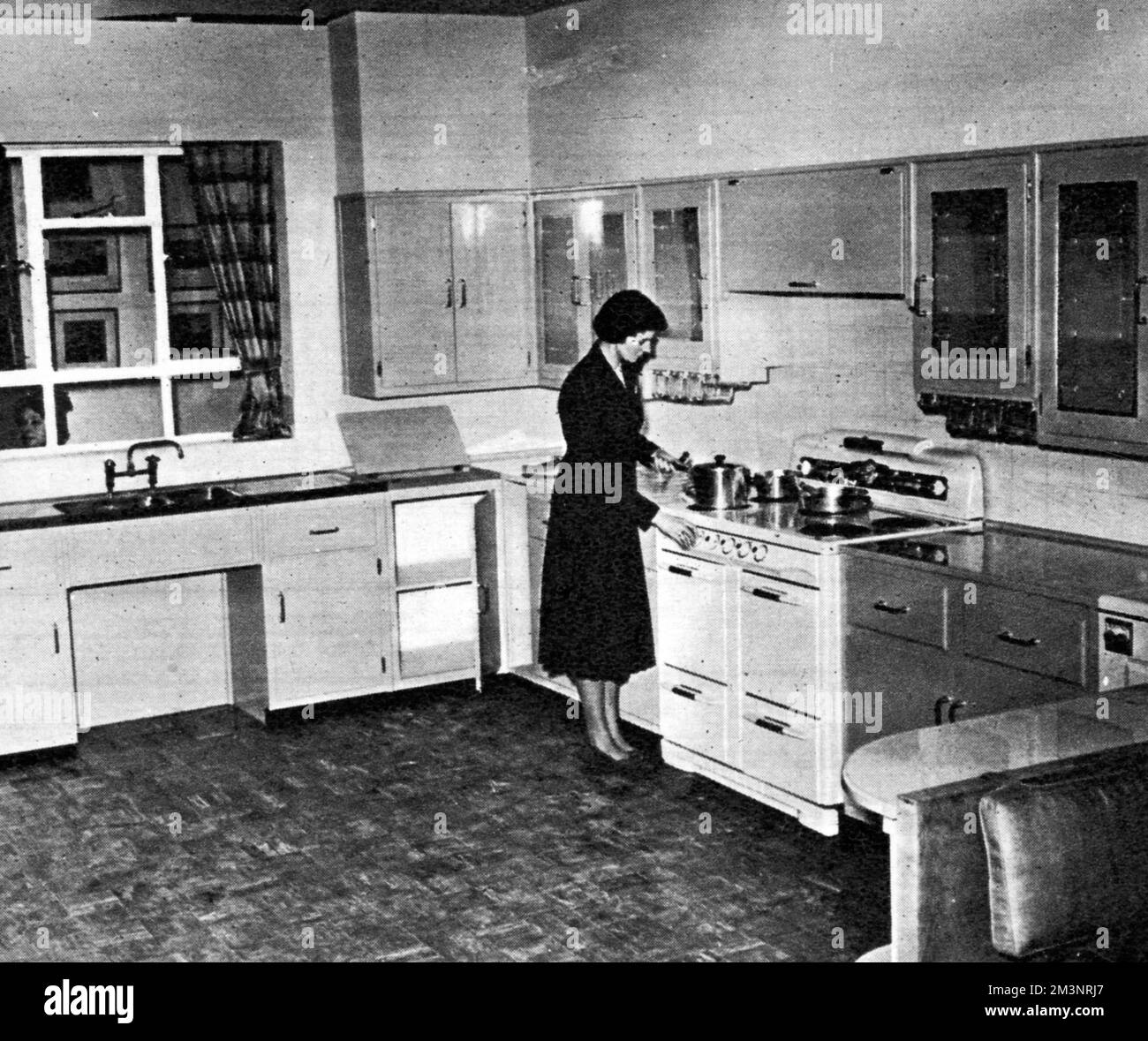 A kitchen at the Ideal Home Exhibition at Olympia, 1951, featured in a spread in Sport &amp; Country magazine: the country housewife at Olympia; this year's Ideal Home Exhibition has much to interest her. The egg-shell blue fitments are by Peerless, timber-made with smooth cellulose finish and with cream Warerite tops. The electric cooker is by Moffat, the refrigerator by Prestcold, and the automatic washing-machine by Bendix. Rubbalux rubber tiles cover the floor.     Date: 1951 Stock Photo