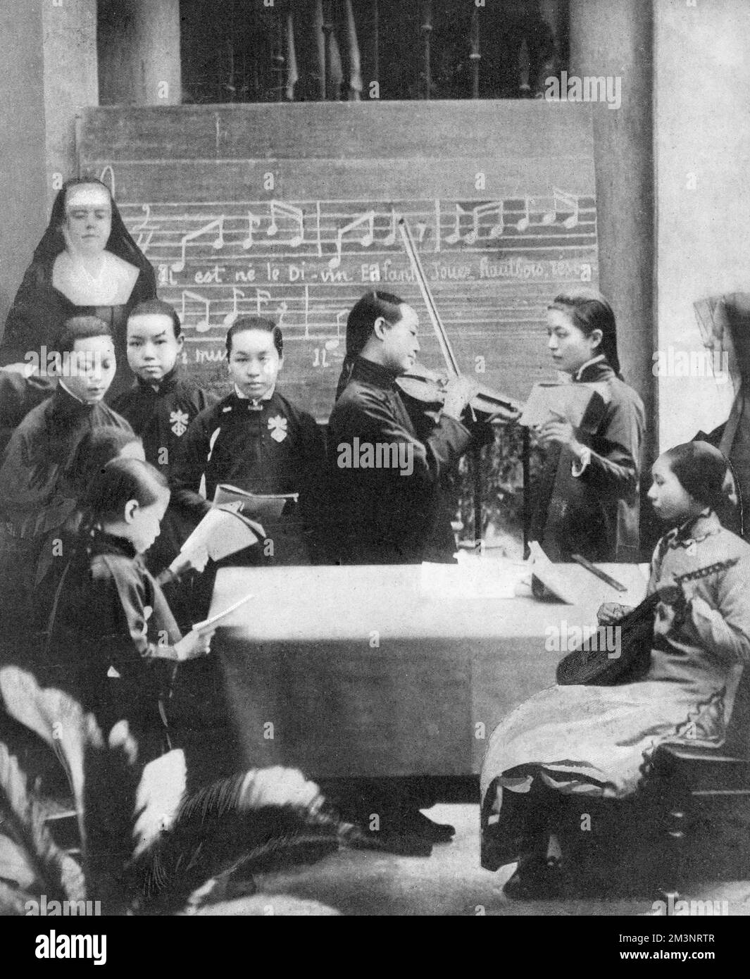 Young Chinese girls at a Roman Catholic school of music in Canton, being taught to play Christmas carols by French nuns.     Date: 1911 Stock Photo