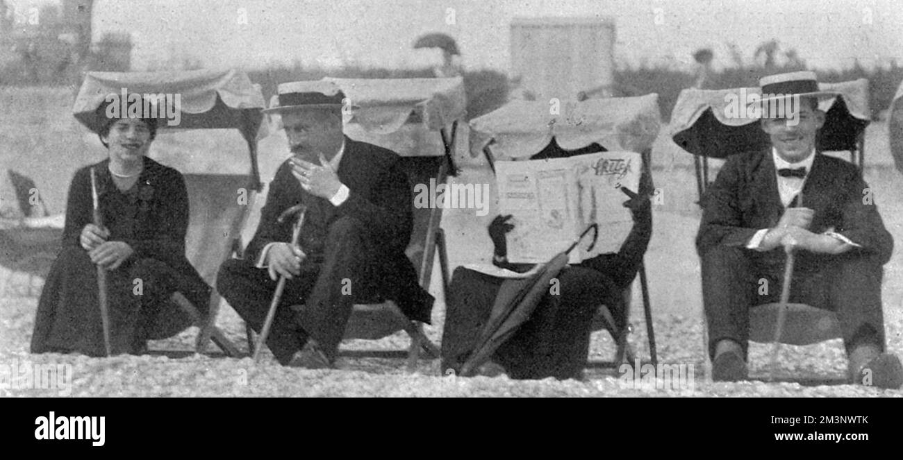 The Queen of Greece, formerly Princess Sophie of Prussia, hides herself from a photographer on the beach at Eastbourne with a copy of The Sketch magazine. Either that or she finds the magazine completely absorbing.  Picture shows, from left, Princess Helen, King Constantine of Greece, Queen Sophie of Greece and Prince Alexander (later King Alexander of Greece).       Date: 1913 Stock Photo