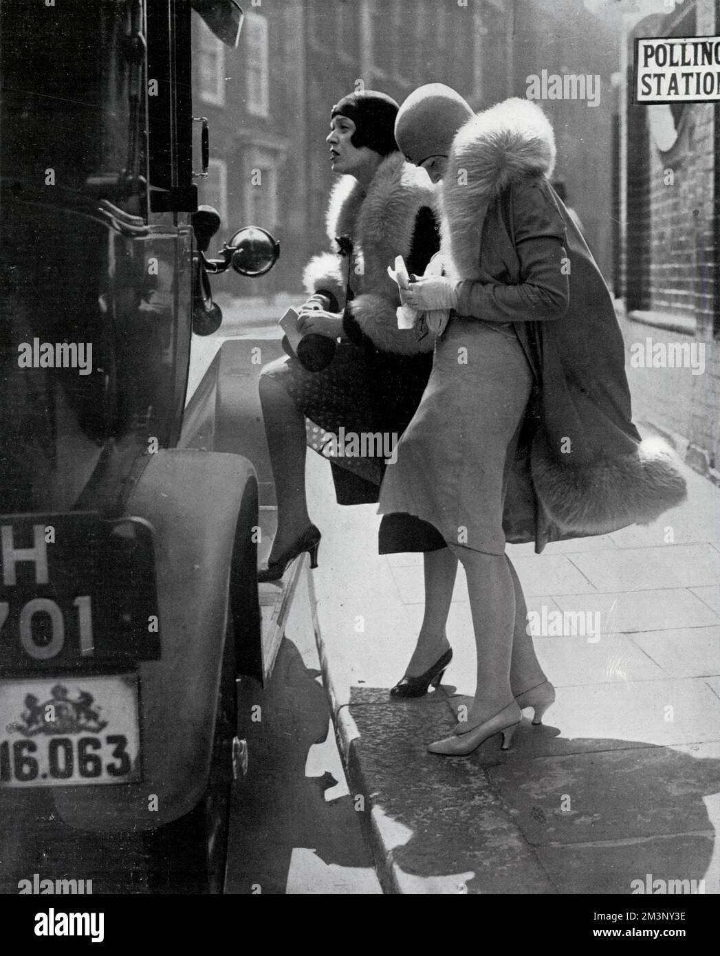 Two sophisticated and fashionable ladies in heels, cloche hats and fur trimmed coats alight from a taxi at a polling station where they will vote for the first time in the General Election of May 1929.  This photograph was accompanied by a caption which may be either humorous, or misogynistically sceptical, but it refers to several ladies who died after the mentally and phyically overwhelming effort of casting their vote!     Date: May 1929 Stock Photo
