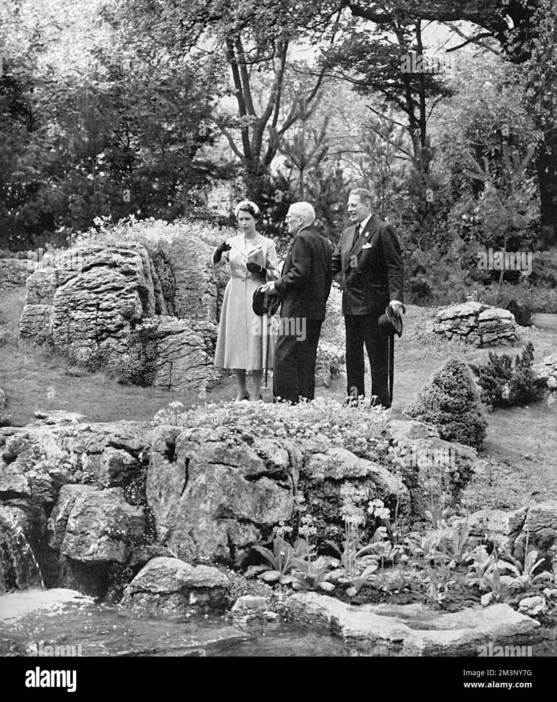 Queen Elizabeth II visiting the Chelsea Flower Show in 1955, inspecting a rock garden feature that has taken her attention.  She is conducted around the show by her maternal uncle, the Hon. David Bowes-Lyon.     Date: 1955 Stock Photo