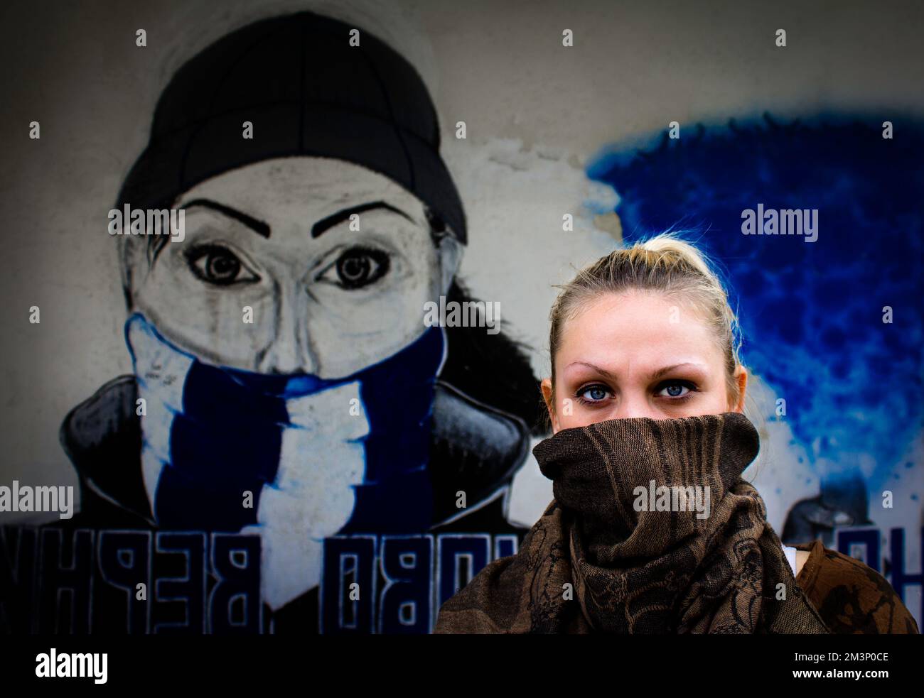 A young female with a mask standing near street art that looks like her in Kumanovo, Macedonia Stock Photo