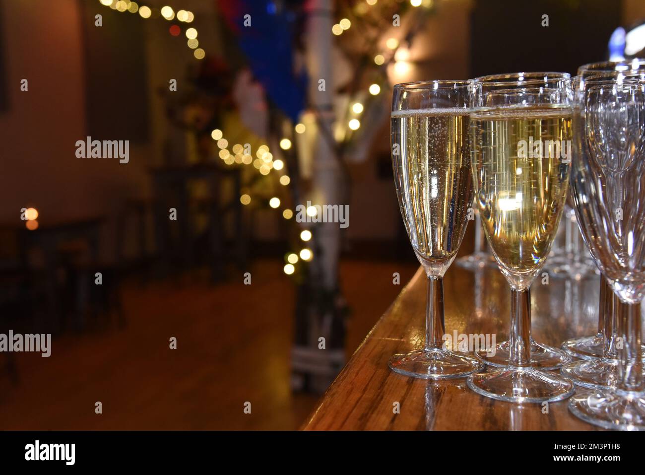 Sparkling white wine in champagne flutes on a bar with soft focus fairy lights in the background and room for copy space Stock Photo