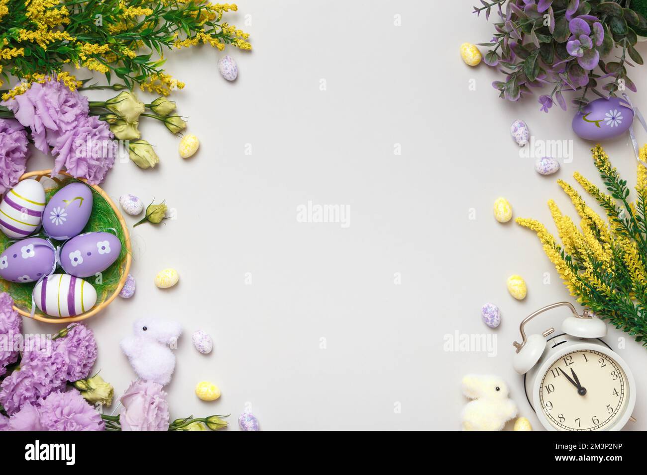Easter composition. Violet and yellow flowers eggs in a basket alarm clock. Stock Photo