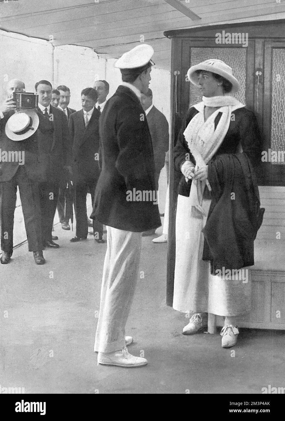 Who Would Be King?  Photograph of King Alfonso XIII of Spain, captured by snapshotters during a trip to San Sebastien, talking to an unidentified young woman.  The Bystander captions the picture with quiet outrage saying, 'Our sympathies to his majesty, King Alfonso.  He cannot even converse with a pretty woman without being surrounded by snapshotters.  This lurid example was itself snapshotted, to our profound regret, during the King's recent visit to San Sebastien.'  They still printed the picture though.     Date: September 1912 Stock Photo