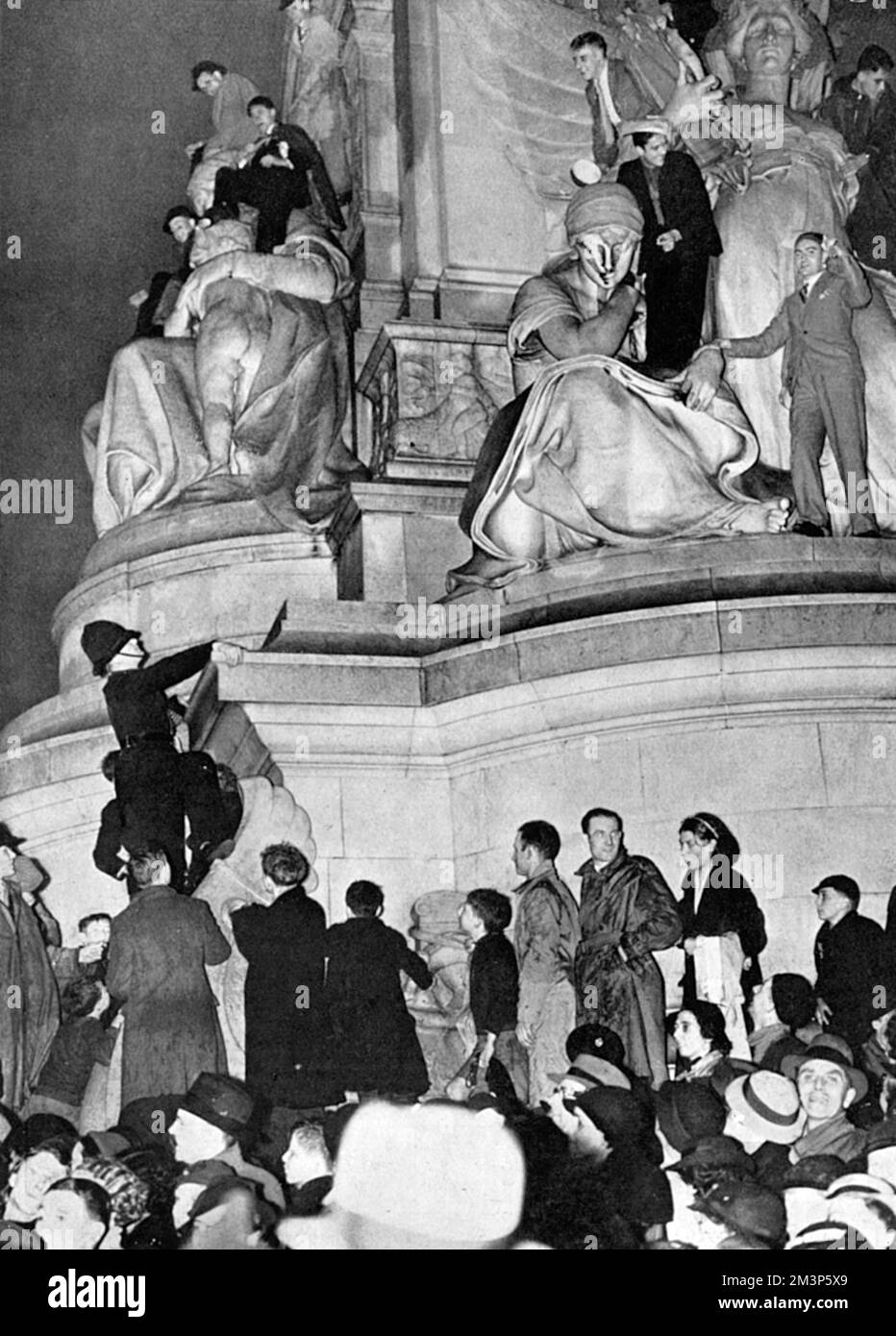 A section of the huge crowd in Trafalgar Square standing by the crush barrier after waiting all night to watch the Coronation procession of King George VI.  By 2am the square was almost full and long before the first procession the gates had to be closed.  Note the policeman in the background, climbing on one of the Trafalgar Square lions, presumably to shoo away climbers!     Date: 1937 Stock Photo