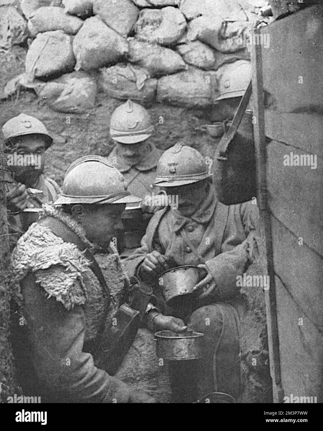 Dinner-time for soldiers in a corner of a fire-trench on the French front in the Argonne. The caption reads: 'The clockwork regularity of the French culinary arrangements at the front, and the food-supply system to the troops in the battlefield region, have been repeatedly remarked on as a wonder of French war organisation'.     Date: 1917 Stock Photo