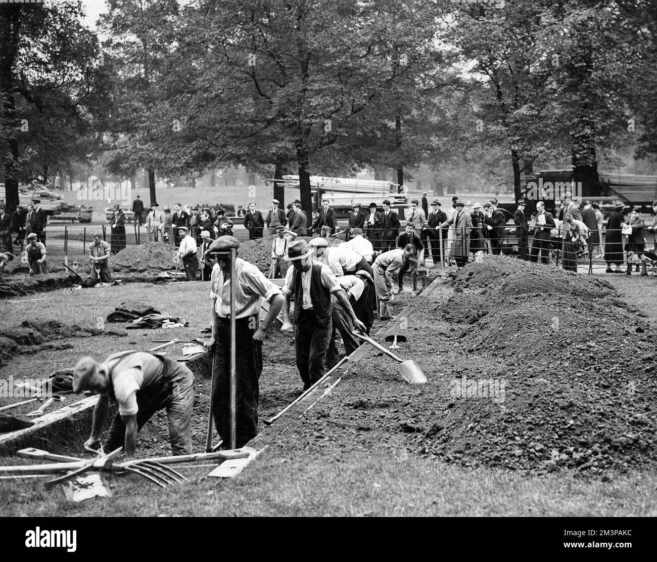 Air Raid Precautions (A.R.P.) volunteers digging trenches and shelters in Kensington Gardens, London, on 26th September 1938, watched by an interested crowd. A.R.P. volunteers were mobilised at this time, and cellars and basements were requisitioned for air raid shelters; trenches were dug in the parks of large towns.     Date: 1938 Stock Photo