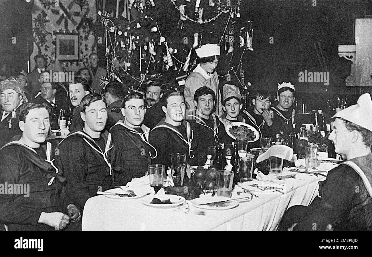 Sailors as guests of Lady Beatty (wife of Admiral Beatty) enjoying a Christmas dinner &quot;somewhere in Scotland.&quot;  The wives of officers of the Grand Fleet helped to make the dinner a success and Mrs Drummond, wife of Captain Drummond, can be seen waiting on the men.  On a platform, or stage beyond the dining tables can be seen a piano and chairs, arranged in anticipation of some imminent festive entertainment.     Date: 1916 Stock Photo