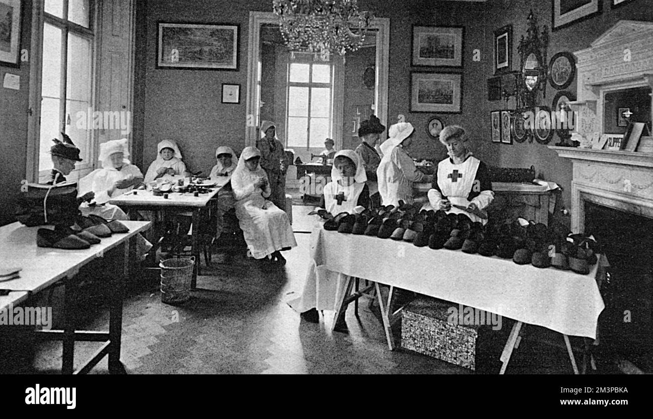 Women at work making slippers in the slipper room of the Marylebone branch of the Red Cross Society which was based in a house in Portman Square lent by Mr Lawson Johnson expressly for the purpose.  The workrooms, staffed entirely by volunteers,  produced garments and surgical requisites for wounded soldiers in hospital and had one room, as shown here, dedicated solely to making slippers.  Many different kinds of slippers were made.  Some of them were made to open at the back so as not to hurt a badly injured foot, while others were made specially big and deep.  The slippers were manufactured Stock Photo