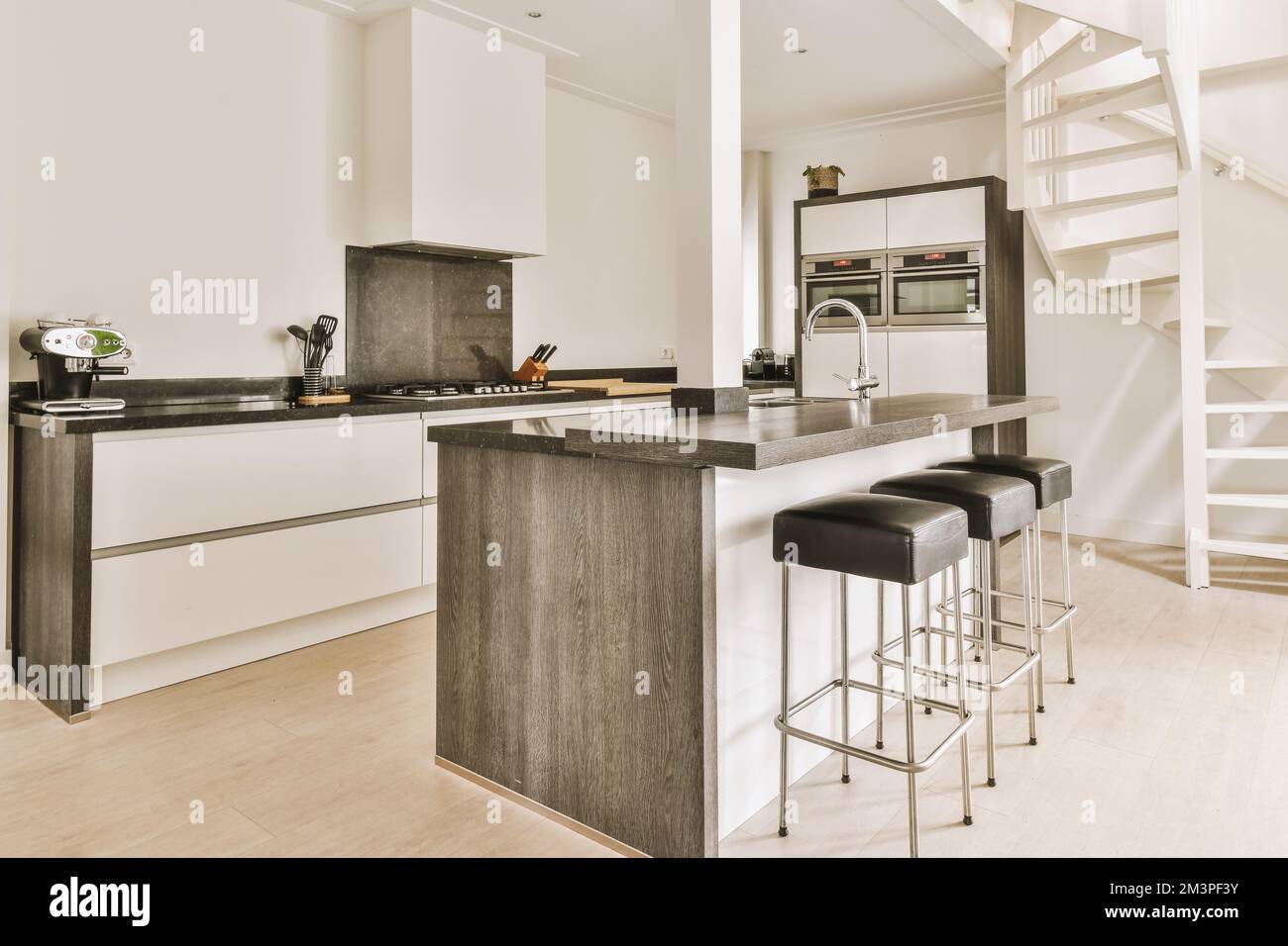 a modern kitchen with white walls and wood flooring, along with stairs ...