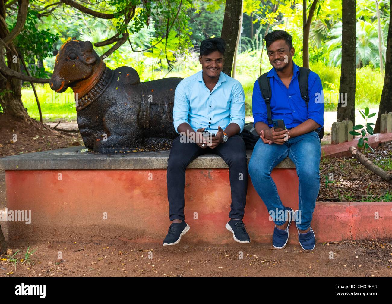 Indian friends sit in a park near a cow statue, Pondicherry, Puducherry, India Stock Photo