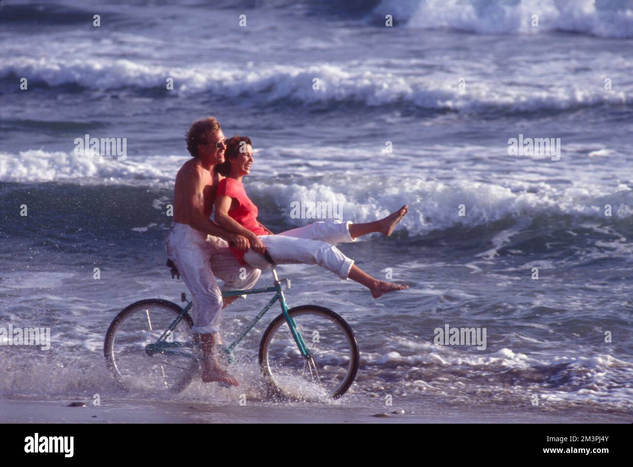 Young couple riding a bike through the surf at the beach Stock Photo
