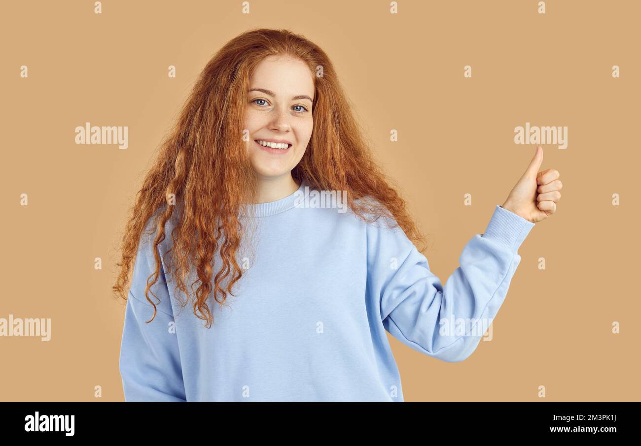 Cute red-haired teen girl raises pointing finger up showing okay gesture, agreement or support. Stock Photo