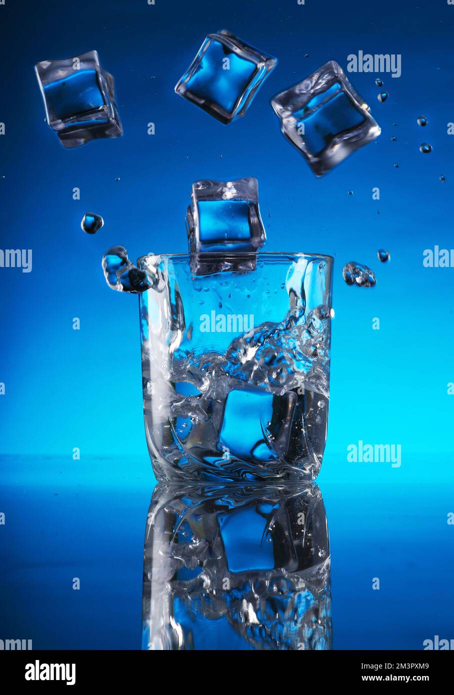 ice cubes falling into a glass of water on a blue background Stock ...