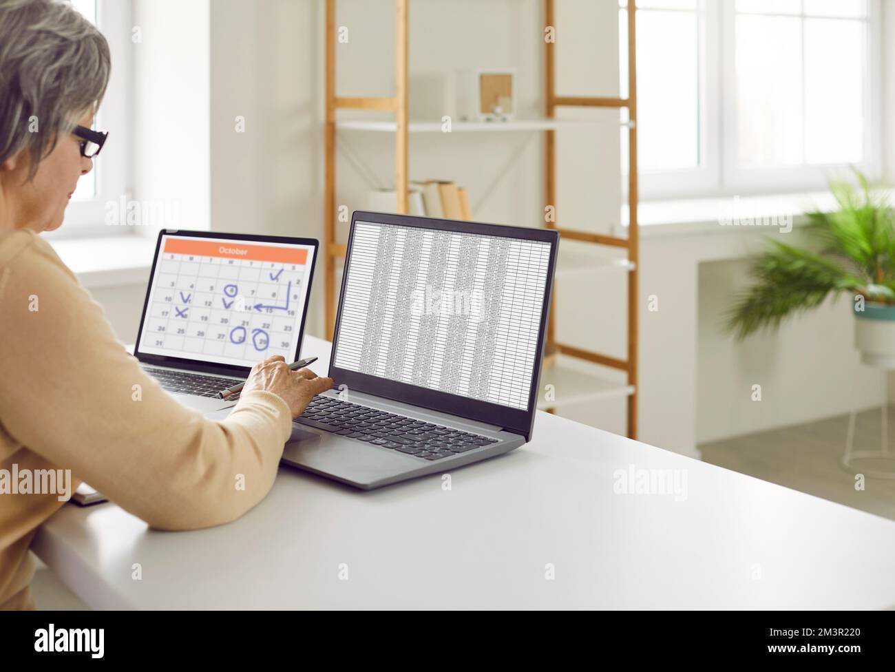 Senior woman using spreadsheets and calendar app on laptop to plan work