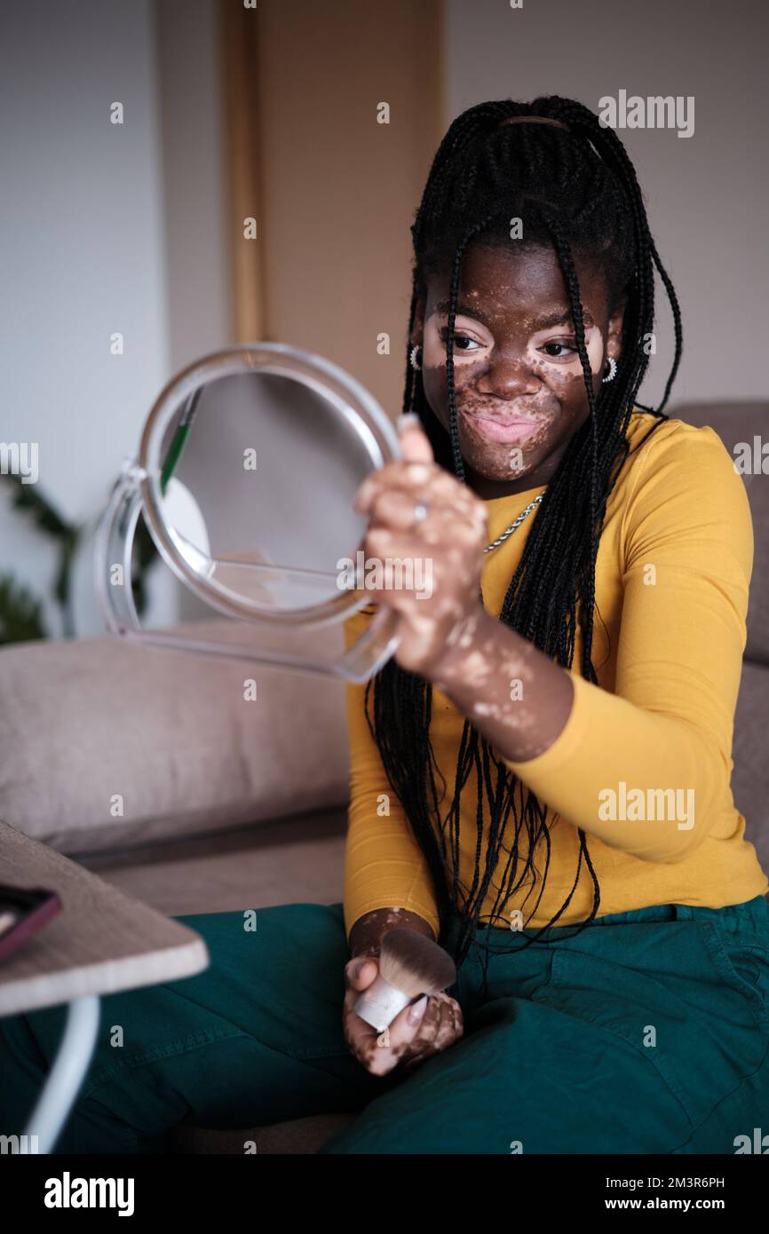 Black woman with vitiligo doing makeup in living room Stock Photo