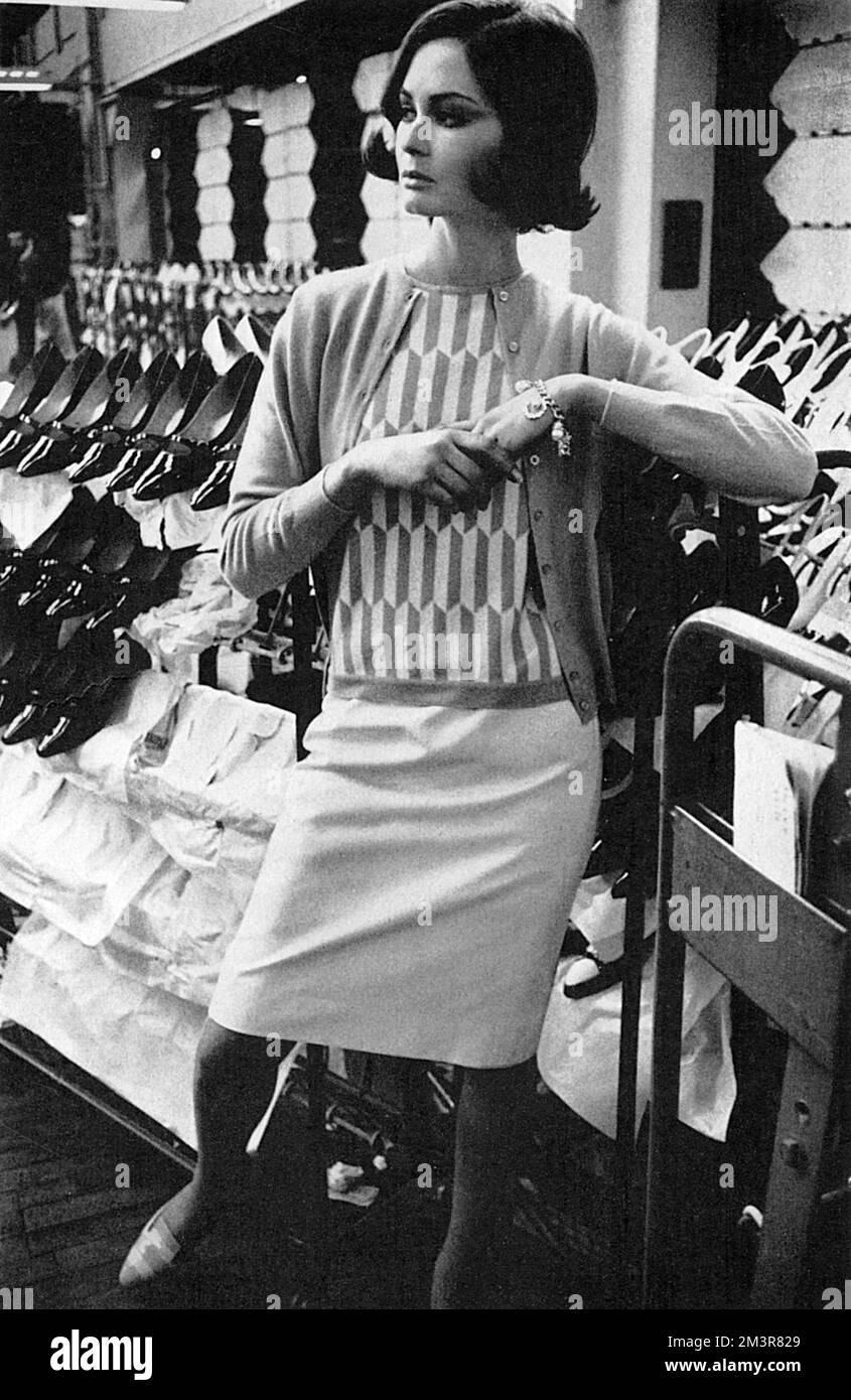 A model wearing cashmere knitwear by Pringle of Scotland, the classic knitwear brand.  The intarsia-patterned sleeveless sweater in pineapple and white is teamed with a classic pineapple cardigan.  Worn with a Terylene and worsted skirt by Daks.  Photographed at Rayne's shoe factory.       Date: 1965 Stock Photo