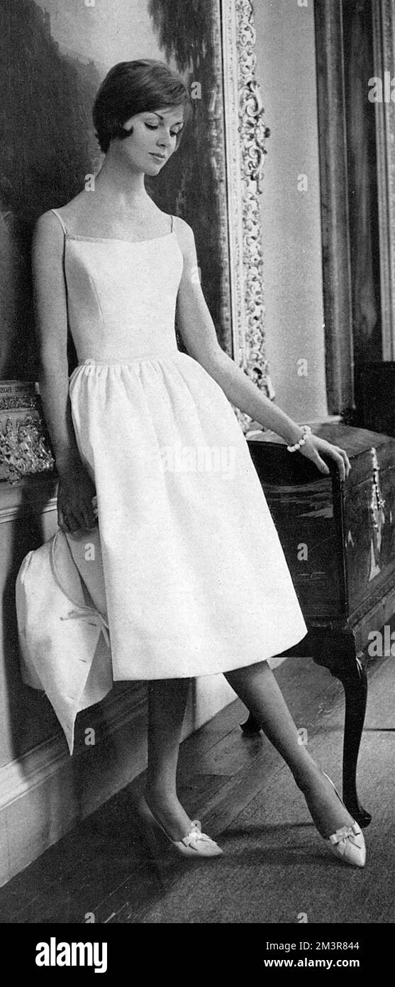 A white pique dress from Horrockses. The full skirt is supported by a stiffened new petticoat, shoe-string shoulder straps and neckline edging are of narrow fondant pink cotton, also used to edge the fitted bolero.     Date: 1961 Stock Photo