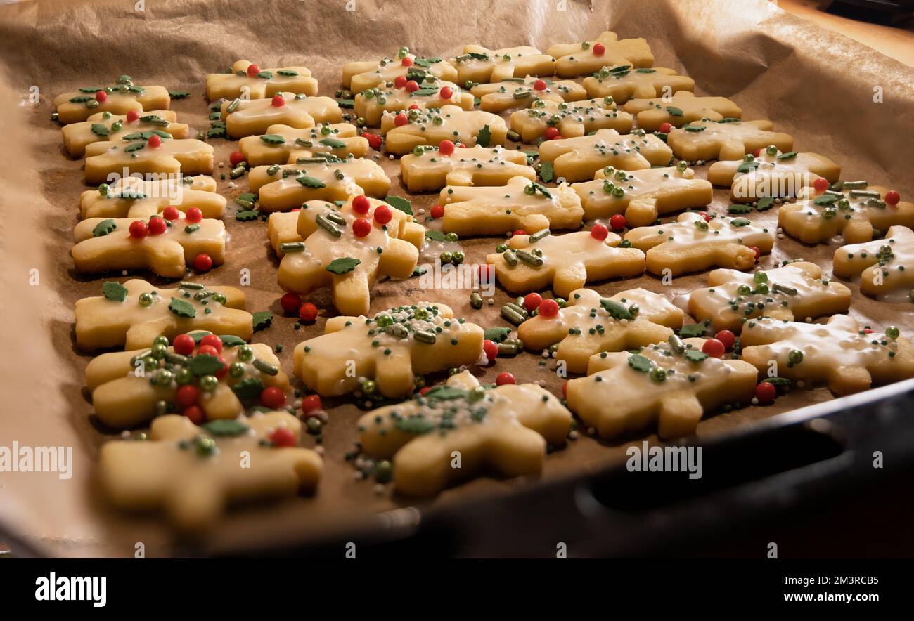 closeup view over a tray of fresh baked homemade christmas cookies, shape of small figures, decorated with sugar coating and colorful sugar beads, bac Stock Photo